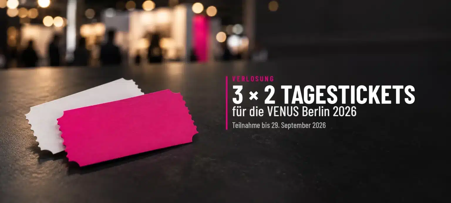 Zwei Eintrittskarten in Magenta und Weiß auf einem dunklen Tisch vor einer unscharfen Messehalle, daneben der Schriftzug „3 × 2 Tagestickets für die VENUS Berlin 2026“